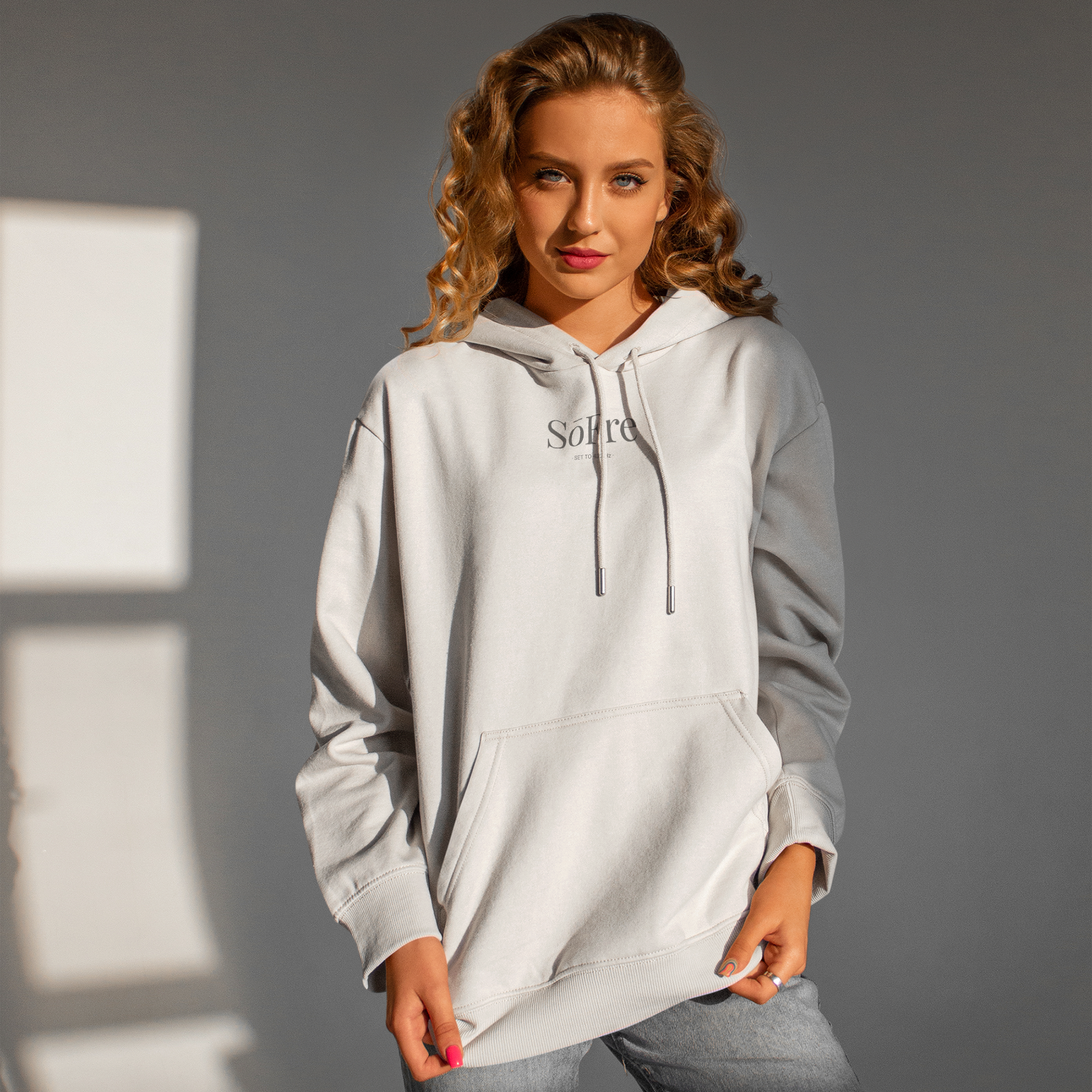 Woman wearing a light gray hoodie with Sofre branding against a neutral background