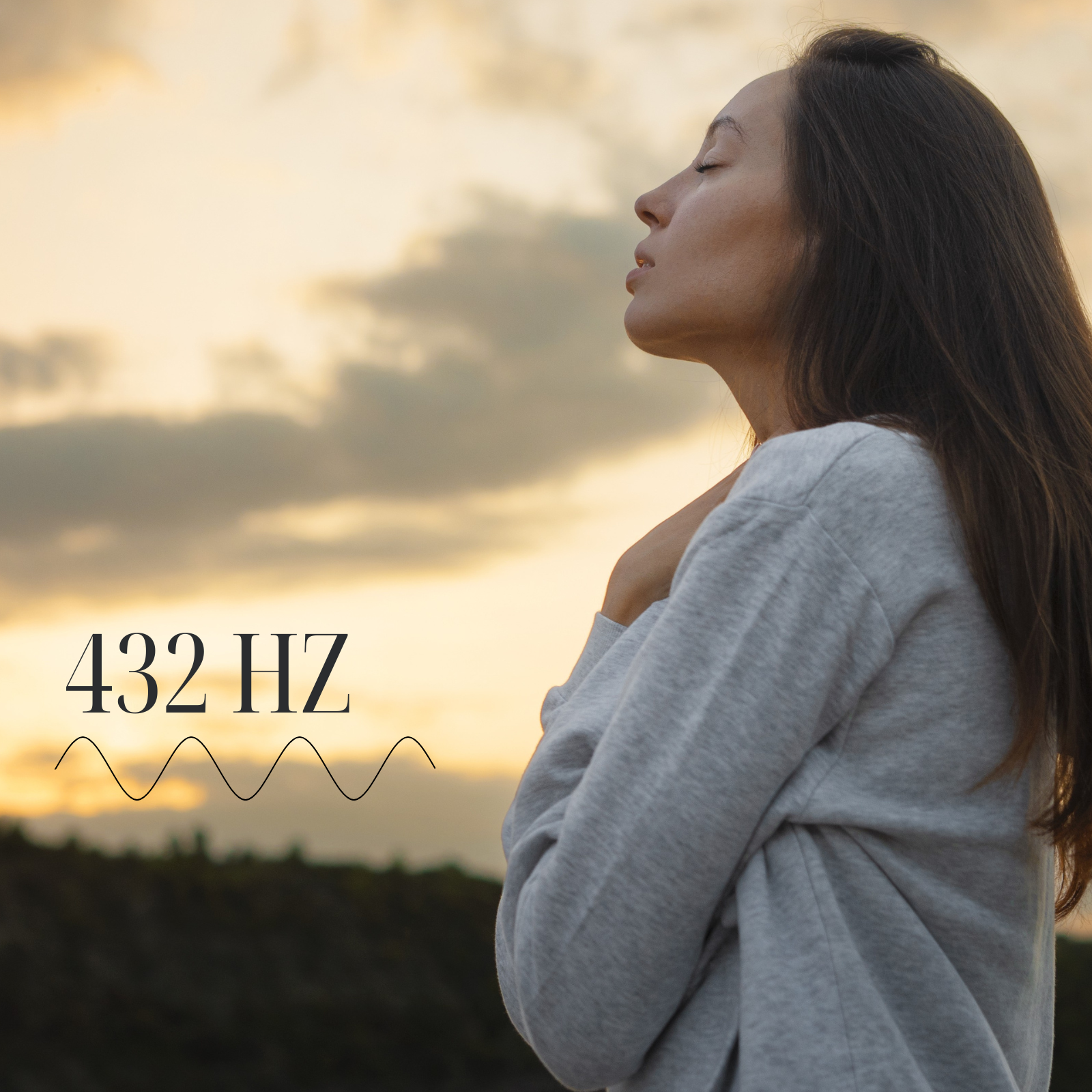 Woman in soft grey sweatshirt standing at sunset with eyes closed, embodying the calming energy of 432 Hz — the healing frequency known to support nervous system alignment and emotional balance.