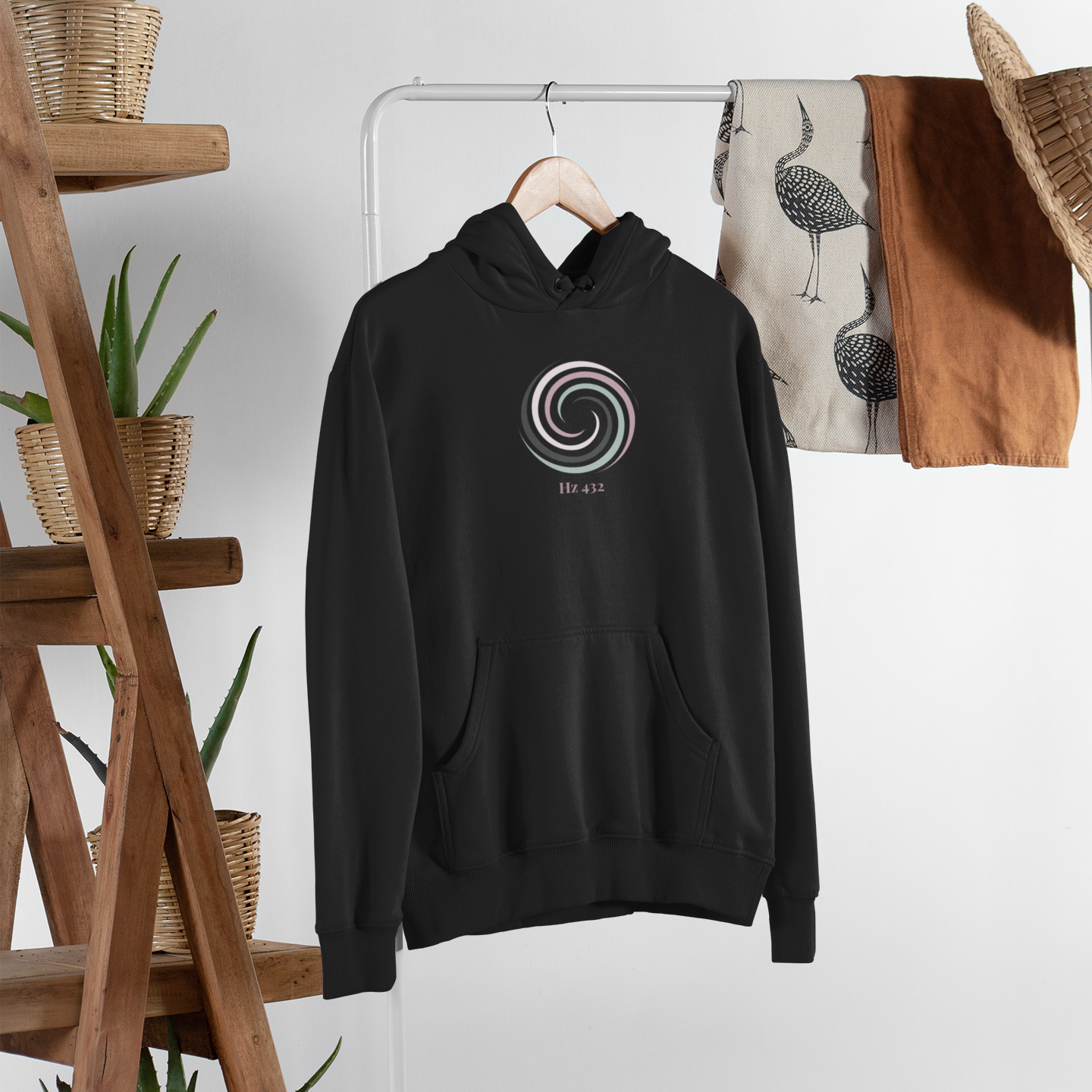 Aura Spiral Hoodie in Eclipse Black hanging on wooden rack — minimalist spiritual apparel with Hz 432 print by Soft Frequencies™